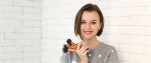 Smiling girl holding makeup brushes